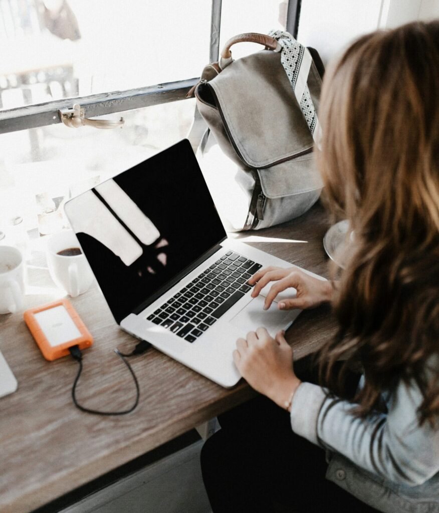Remote professional working on laptop near window with coffee and backpack